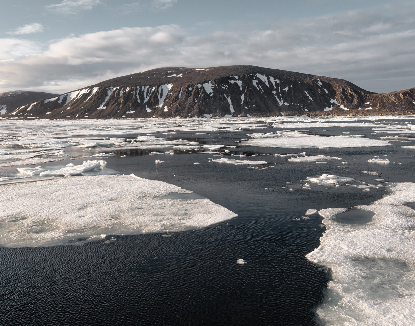 Image of sea ice with a frozen barren moutain island in the background in the Svalbard Archipelago